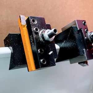 May include: Two black metal tool holders with yellow and silver accents. The tool holder on the left has the number "250-002" printed on it. The tool holder on the right has a silver screw with a black handle.