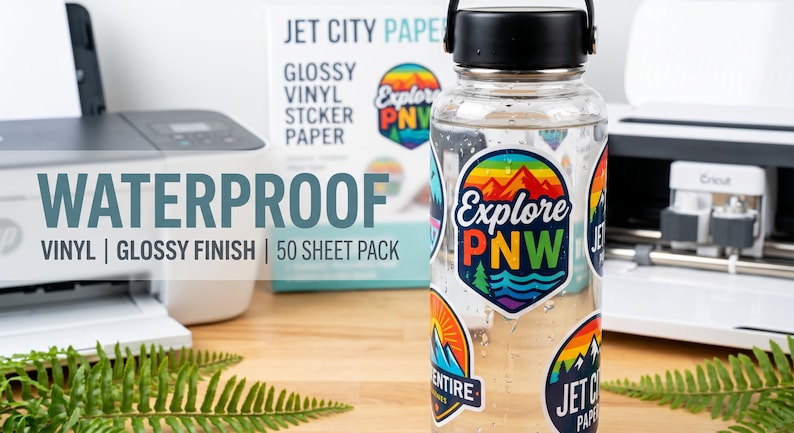 May include: A clear water bottle covered in colorful stickers with the text "Explore PNW." The bottle is next to a box of glossy vinyl sticker paper and a printer. The text "Waterproof Vinyl Glossy Finish 50 Sheet Pack" is also visible.