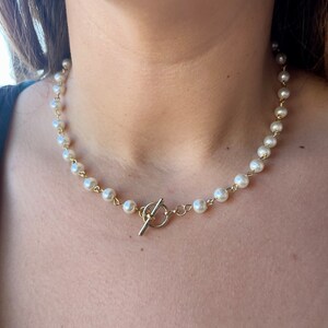 May include: A gold chain necklace with white pearl beads and a gold toggle clasp.