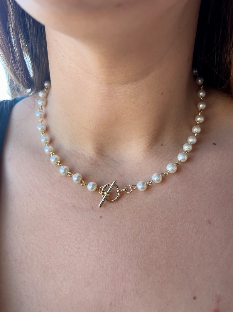 May include: A gold chain necklace with white pearl beads and a gold toggle clasp.