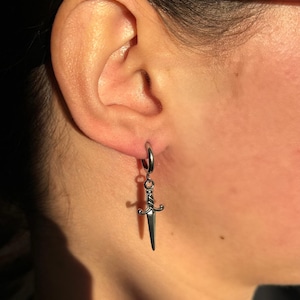 May include: Silver hoop earrings with a dangling silver dagger charm.