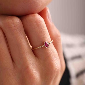 Może przedstawiać: Delikatny złoty pierścionek z żywym owalnym rubinem. Smukła obrączka pierścionka i bogaty czerwony odcień rubinu tworzą klasyczny i elegancki design. Pierścionek to element wysokiej jakości biżuterii.