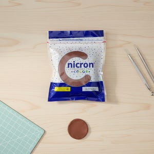 May include: A packet of brown Nicron cold porcelain clay with a large letter "C" shape, a small clay circle, and two metal tools. The package is white with blue accents and the text "nicron" and "color". The clay is 250g.