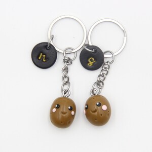 May include: Two brown potato-shaped keychains with happy faces. Each keychain has a black circle charm with a gold letter, one says "N" and the other says "S".