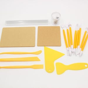 May include: A set of yellow and white polymer clay sculpting tools. The set includes a variety of tools for shaping, smoothing, and detailing clay. The set also includes two brown square tiles and a clear acrylic roller.