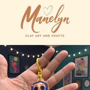 May include: A Coraline-themed keyring featuring a doll with button eyes, wearing a yellow coat and blue hair. The keyring is attached to a yellow ring. The image also shows a matching bag and the text "Cute Coraline Keychain For Every Spooky Girl".