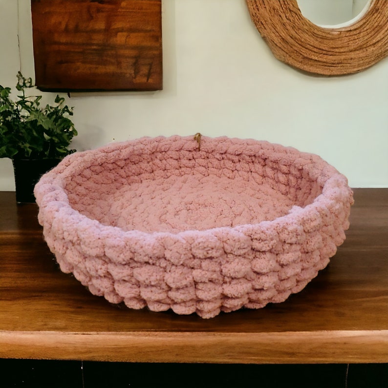 May include: A pink crocheted pet bed with a round shape and a textured surface.