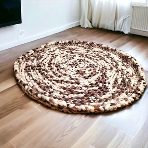May include: A round, brown and cream colored braided rug with a circular pattern. The rug is made of thick, textured yarn and has a slightly raised edge.