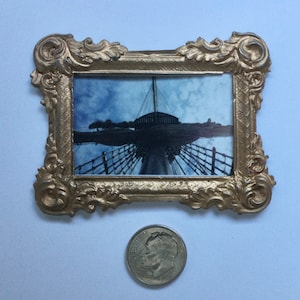 May include: An ornate picture frame in gold with a detailed design. The frame contains a photograph of a ship's mast and rigging.