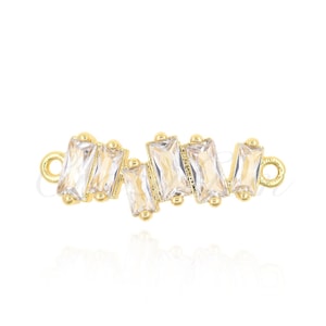 Puede incluir: Un componente de joyería dorado con una serie de cristales rectangulares transparentes. Los cristales están dispuestos en un patrón en zigzag y engastados en metal dorado. El componente tiene pequeños bucles en cada extremo para la fijación, adecuado para la fabricación de joyas.
