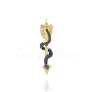 Peut inclure: Un charme de flèche en or avec un serpent noir enroulé autour. La flèche est pointue et a une ailette décorative en haut.