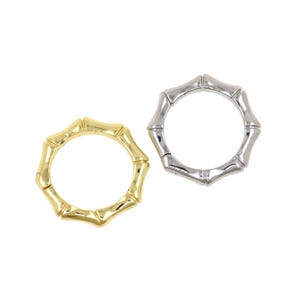 Può includere: Due anelli in stile bambù, uno dorato e uno argentato, sono presentati su sfondo bianco. Gli anelli hanno un design segmentato, che imita l'aspetto degli steli di bambù. L'anello dorato è a sinistra, l'anello argentato a destra.
