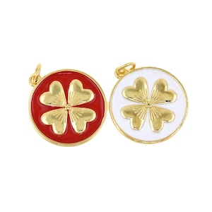 Puede incluir: Dos colgantes redondos con un diseño de trébol de cuatro hojas. Uno tiene un fondo rojo con un trébol dorado, y el otro tiene un fondo blanco con un trébol dorado. Ambos tienen un lazo dorado para colgar.
