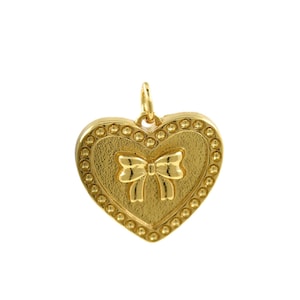以下が含まれることがあります： ビーズの縁取りが施された、ゴールドのハート型のペンダント。ペンダントには、立体的なボウのデザインが施されています。