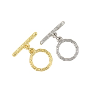 May include: Two toggle clasps, one gold-toned and one silver-toned, are displayed against a white background. Each clasp features a textured bar and a textured ring. The clasps are designed for jewelry making and crafting.