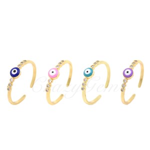 May include: Four gold adjustable rings with a single evil eye charm in blue, pink, turquoise, and purple. Each ring is adorned with clear cubic zirconia stones.