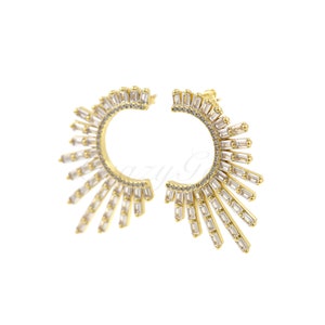 May include: Gold hoop earrings with a sunburst design featuring clear cubic zirconia stones.
