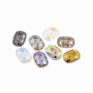 Op de afbeelding: Assortiment van acht twee-gaats kristallen knopen in verschillende kleuren, waaronder helder, bruin, goud en iriserend.