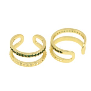 May include: Two gold ear cuffs with a double band design. Each band is decorated with a row of small green gemstones.