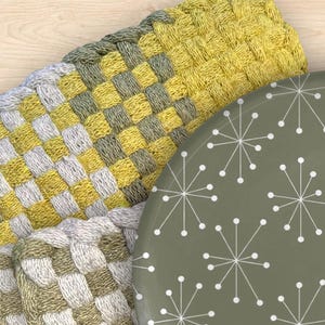 May include: Close-up of woven trivets in yellow, gray, and white. A round, olive-green plate with a white starburst pattern is partially visible. The trivets have a textured, checkered design, suitable for kitchen use.