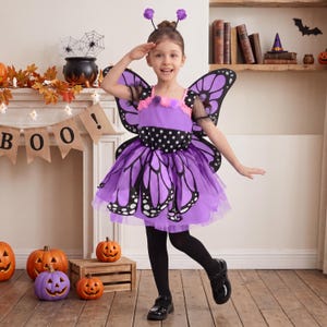 May include: A purple butterfly costume featuring a bodice with black and white polka dots, a layered tulle skirt with black butterfly wing patterns, matching black butterfly wings, and a headband with two purple pom-poms on thin wire antennae.