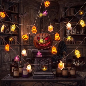May include: A string of Halloween-themed LED lights featuring various shapes including orange pumpkins, white ghosts, purple witch hats, green bats, and spider webs. The lights are illuminated and connected by a thin white wire, creating a festive display.
