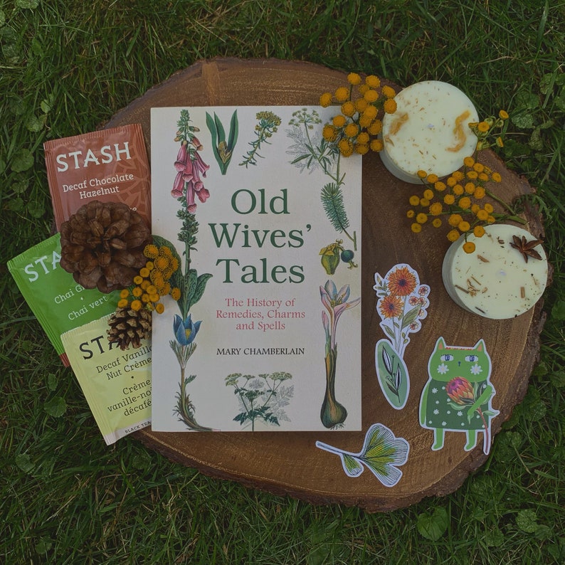 Puede incluir: Un libro titulado "Old Wives' Tales: The History of Remedies, Charms and Spells" de Mary Chamberlain, con una ilustraci&oacute;n floral en la portada. El libro est&aacute; rodeado de bolsitas de t&eacute;, peque&ntilde;os jabones redondos y pegatinas decorativas con dise&ntilde;os florales y de gatos.