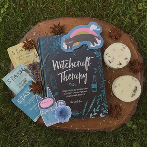 Puede incluir: Un libro negro con el t&iacute;tulo "Witchcraft Therapy: Your Guide to Banishing Bullsh*t and Invoking Your Inner Power" de Mandi Em. El libro est&aacute; rodeado de bolsitas de t&eacute;, velas y pegatinas decorativas.