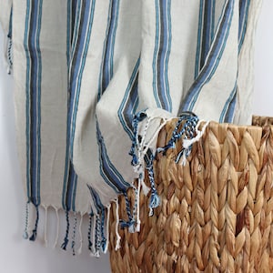 May include: A woven basket with a natural brown color and a wooden handle. A striped throw blanket with blue and white stripes hangs over the edge of the basket.