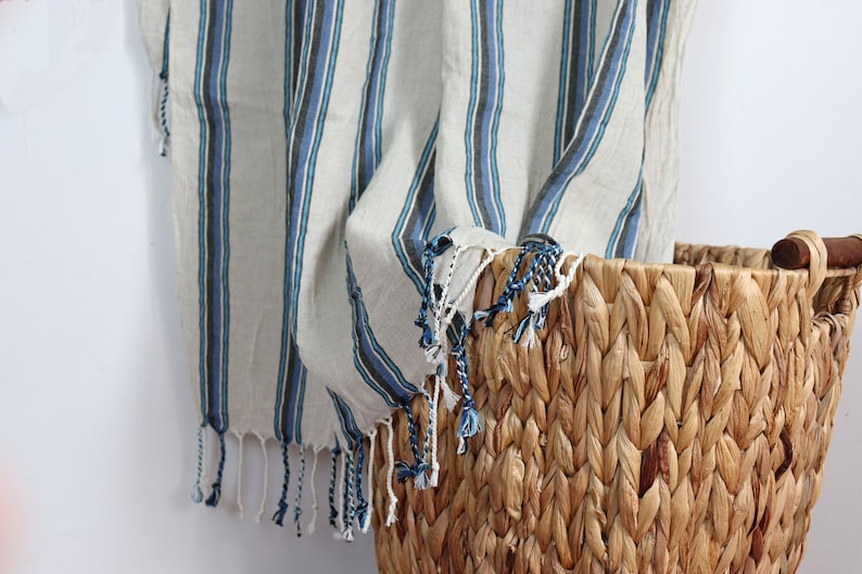 May include: A woven basket with a natural brown color and a wooden handle. A striped throw blanket with blue and white stripes hangs over the edge of the basket.