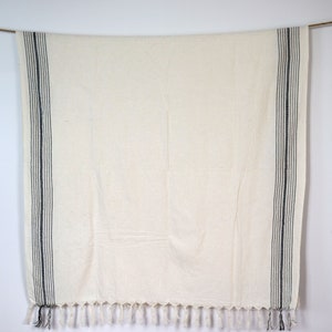 May include: A white throw blanket with black stripes and fringe. The blanket is hanging from a string.