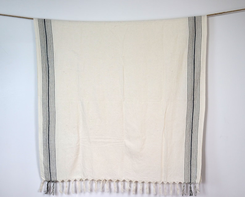 May include: A white throw blanket with black stripes and fringe. The blanket is hanging from a string.