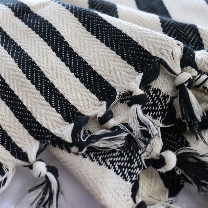 May include: Black and white striped throw blanket with fringe tassels. The blanket is made of a soft, woven fabric.
