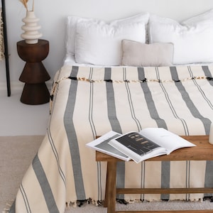 May include: A white bed with black and white striped bedding. The bedding has a fringe trim. A magazine is on a wooden stool in front of the bed.