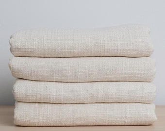 May include: A stack of four folded pieces of off-white, textured fabric. The material features a visible, coarse weave with a natural, unbleached appearance. Each layer is neatly stacked, showing consistent thickness and a woven textile pattern.