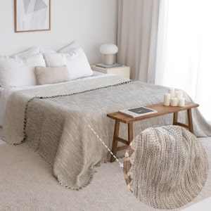 May include: A gray and white throw blanket with a fringe border. The blanket is made of a soft, textured fabric and has a subtle striped pattern.