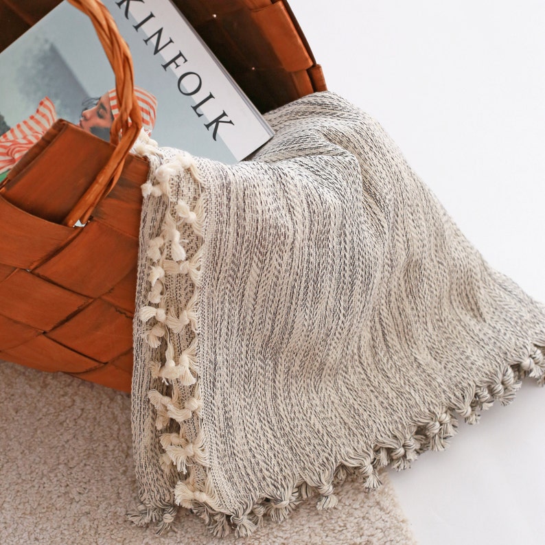 May include: A white and black striped throw blanket with fringe trim. The blanket is folded and placed in a woven basket.