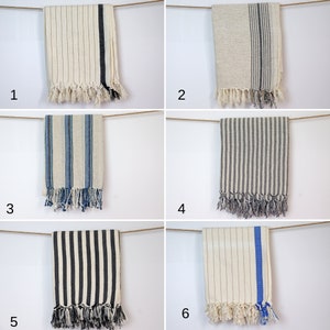 May include: Six different striped towels hanging on a clothesline. The towels are all white with different colored stripes. The towels are all fringed on the bottom.