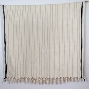 May include: A white throw blanket with black stripes and fringe. The blanket is hanging from a string.