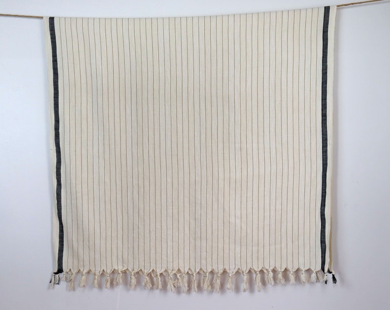 May include: A white throw blanket with black stripes and fringe. The blanket is hanging from a string.