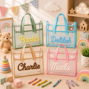 May include: Four rectangular clear plastic tote bags with fabric trim and handles. Each bag features a name in raised script lettering: Peadar in yellow, Delilah in blue, Charlie in brown, and Maela in white. The bags have white snap closures.