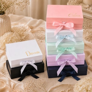 May include: A stack of colorful gift boxes in pink, white, mint green, lavender, and navy blue, each with a matching satin ribbon bow. The boxes are personalized with gold lettering, with names like "Eileen" and "Darren".