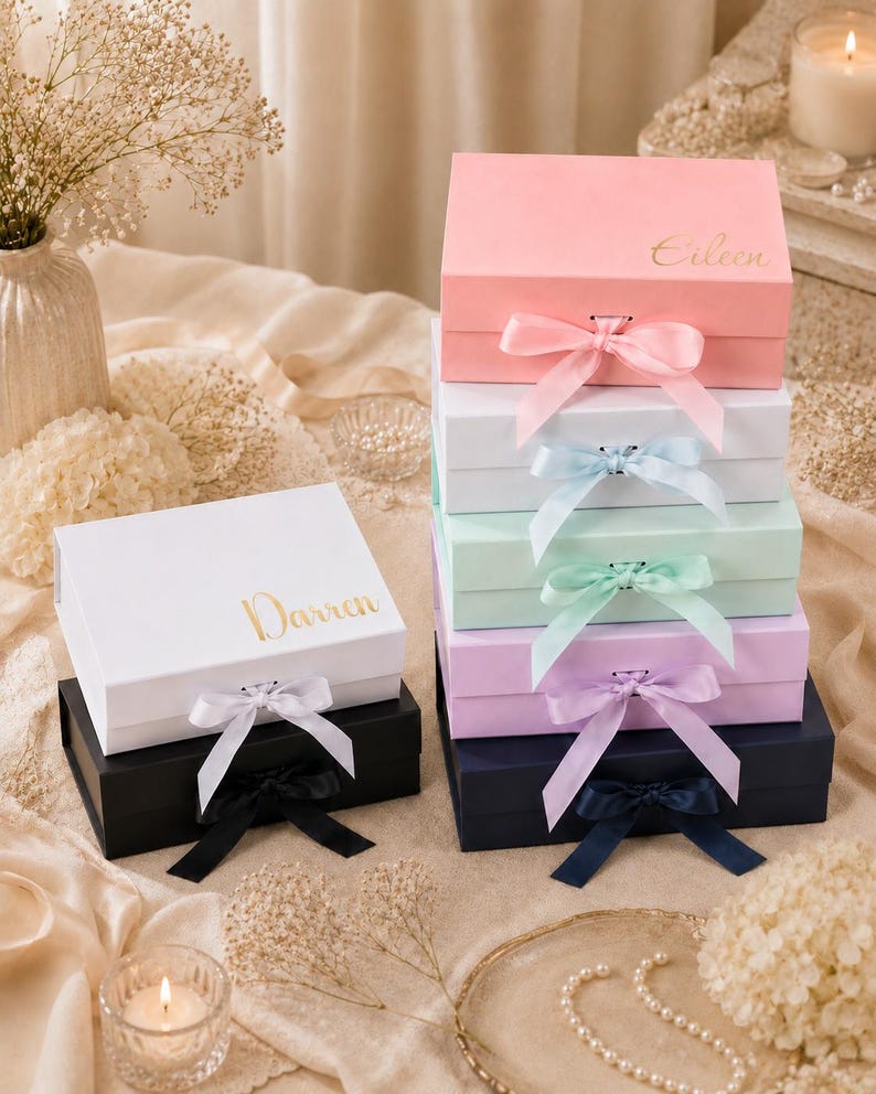 May include: A stack of colorful gift boxes in pink, white, mint green, lavender, and navy blue, each with a matching satin ribbon bow. The boxes are personalized with gold lettering, with names like "Eileen" and "Darren".