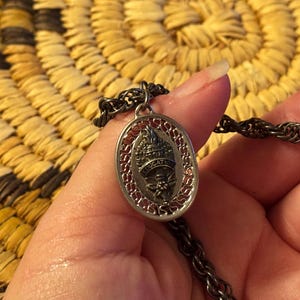 May include: Silver-toned oval pendant necklace with a detailed design. The pendant features a central emblem with the word "EDUCATION" and a decorative border. The chain is a dark, twisted rope style.