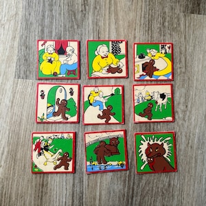 May include: Eight colorful illustrated square tiles depicting a gingerbread man, a woman knitting, a woman baking, a woman with a gingerbread man, a man with a gingerbread man, a woman with a gingerbread man, a woman with a gingerbread man, and a gingerbread man with a wolf.