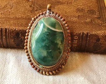 May include: A green agate stone pendant with a silver and copper setting. The pendant is oval shaped and has a white swirl in the center of the stone.