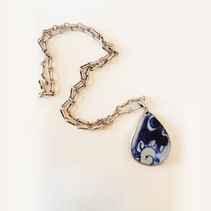 Può includere: Una collana a catena d'argento con un ciondolo a forma di lacrima. Il ciondolo è in porcellana blu e bianca con un motivo floreale.