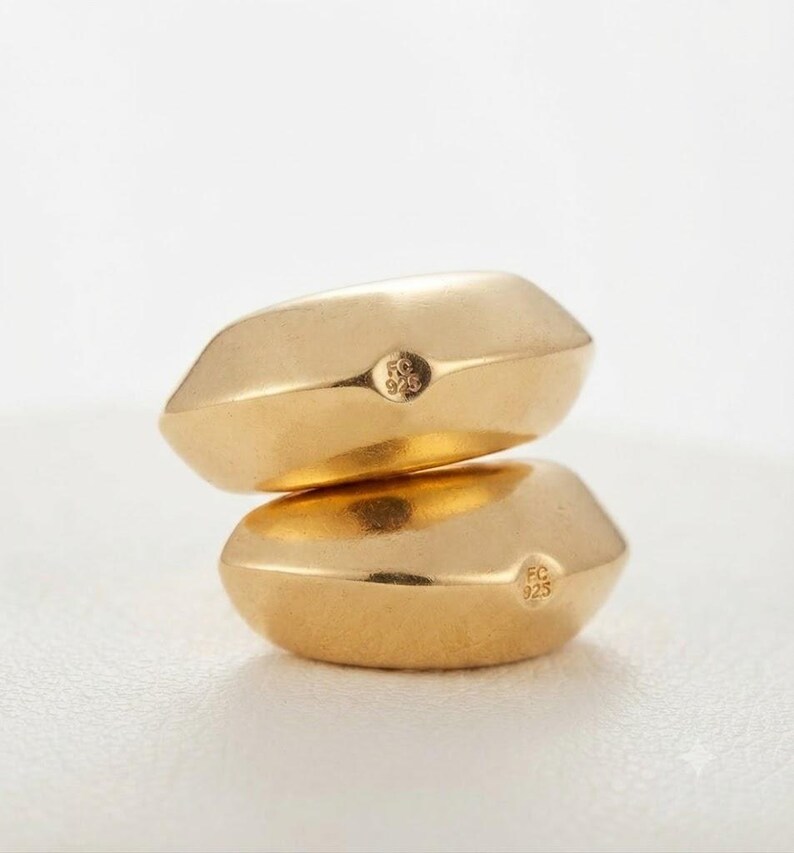 May include: Two gold-toned rings with a smooth, faceted, pebble-like shape stacked vertically. Each ring features a small circular hallmark stamped on the side with the text FC 925, indicating sterling silver construction with a gold finish.