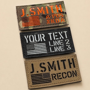 May include: Three rectangular morale patches with hook-and-loop backing. The top patch features camouflage fabric with orange text J. SMITH and A POS NKDA. The middle patch is black with white text YOUR TEXT LINE 2 LINE 3. The bottom is tan with black text J. SMITH RECON.