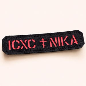 以下が含まれることがあります： 角が斜めにカットされた長方形の黒い布製パッチ。赤い文字で「ICXC NIKA」と中央に赤い正教会の十字架がデザインされています。黒い素材からデザインが切り抜かれており、表面の下から鮮やかな赤い層が見えています。